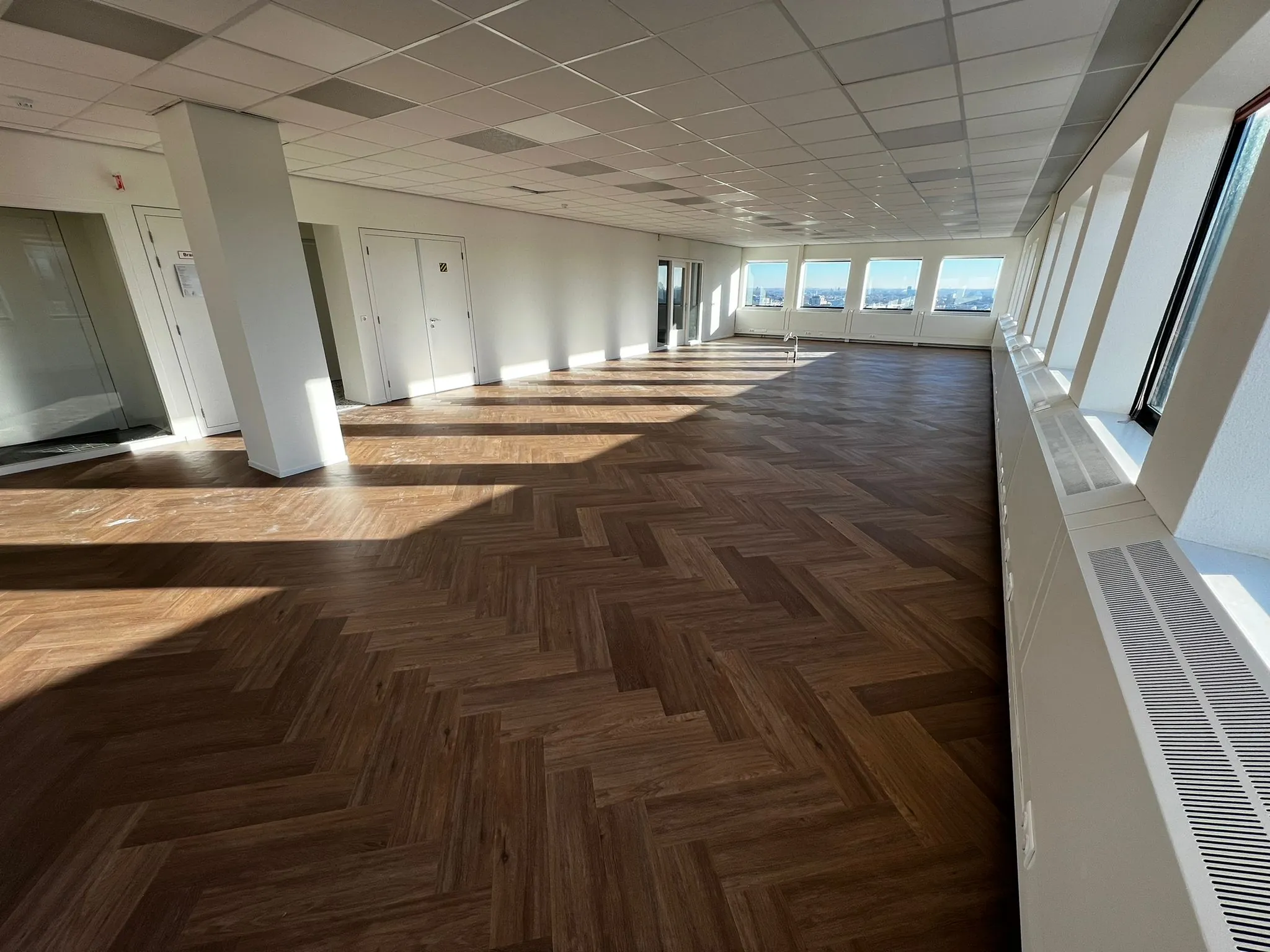 Lichte, lege kantoorruimte aan het Johanna Westerdijkplein met visgraatvloer en grote ramen.